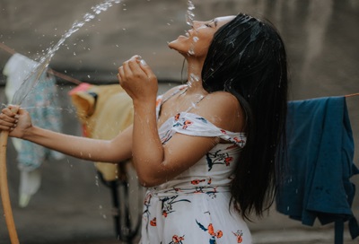 An image of a woman dripping herself in water from a hose..