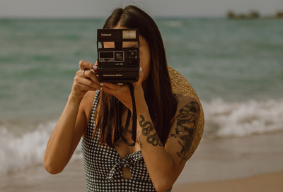 A woman sitting on the sand while taking a photograph.