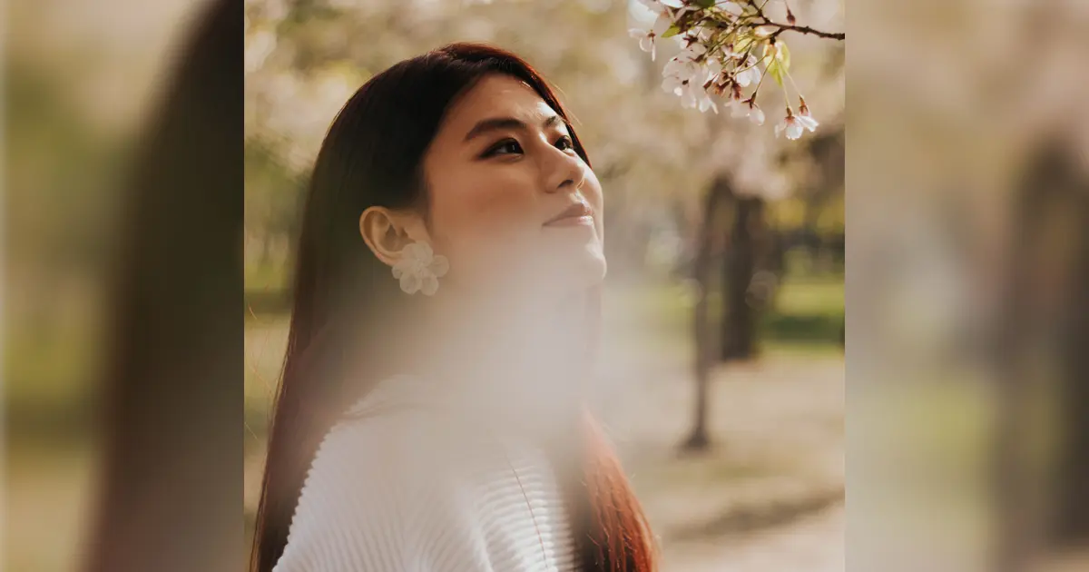 A photo of an Asian woman standing near a tree.