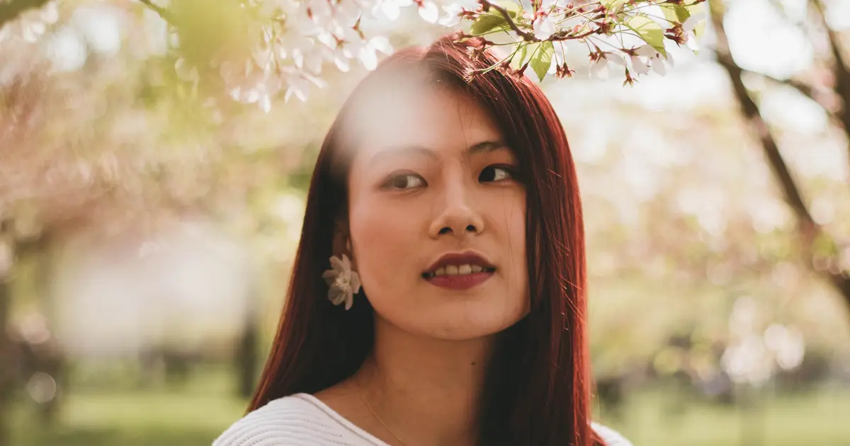 A photo of an Asian woman smiling under the trees.