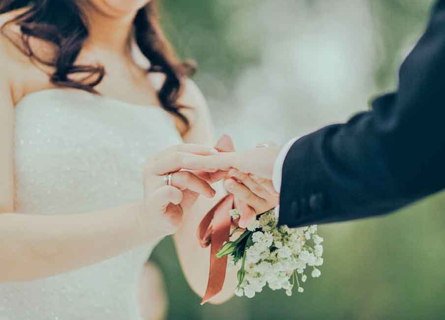 A photo of a bride inserting the wedding ring on the groom’s finger. 